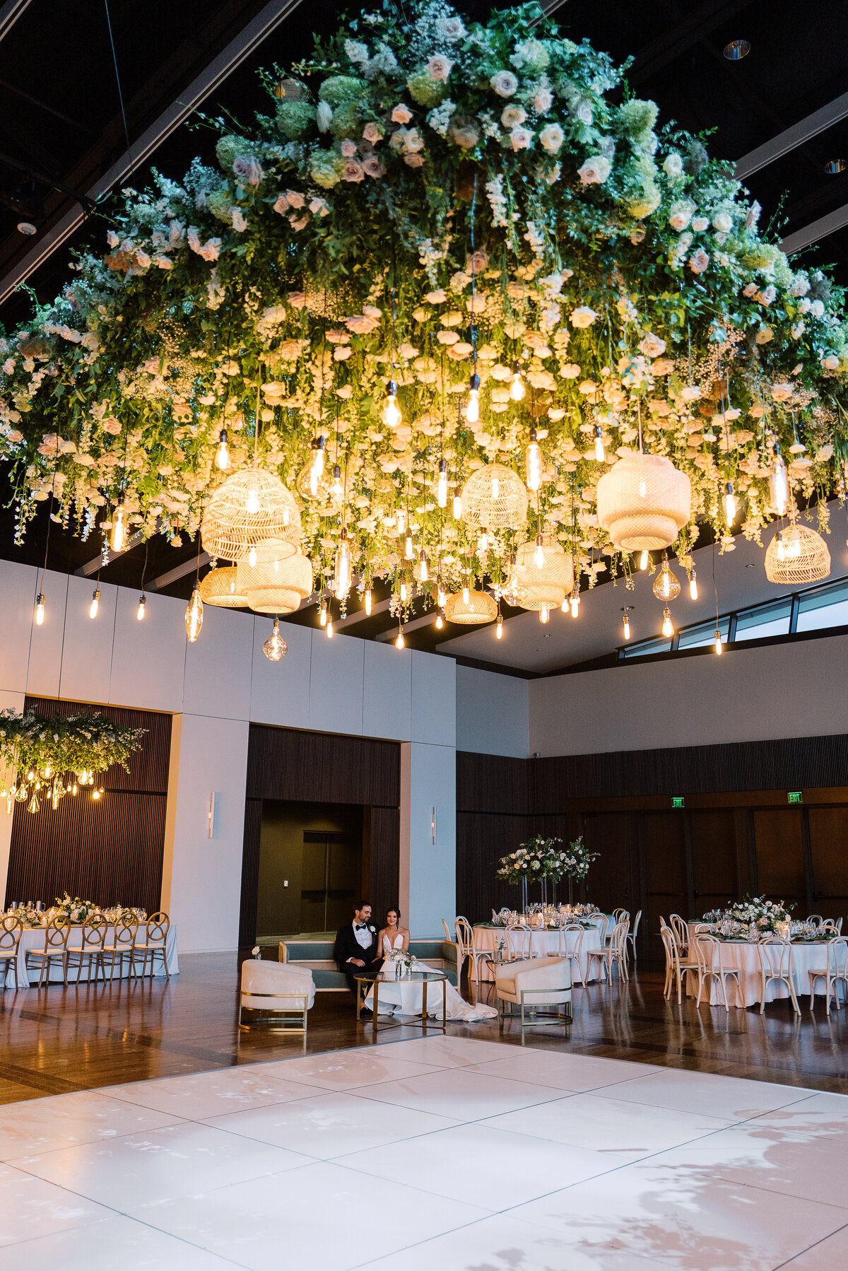 Large dance floor floral installation for classic summer wedding in downtown Nashville. Timeless floral design highlights this garden-inspired wedding reception. Hanging flowers and rattan chandeliers create lush floral dance floor moment. Classic white and green wedding with floral colors in cream, white, taupe, and champagne. Summer floral design full of roses, ranunculus, hydrangea, cosmos, and lisianthis. Design by Rosemary & Finch Floral Design.