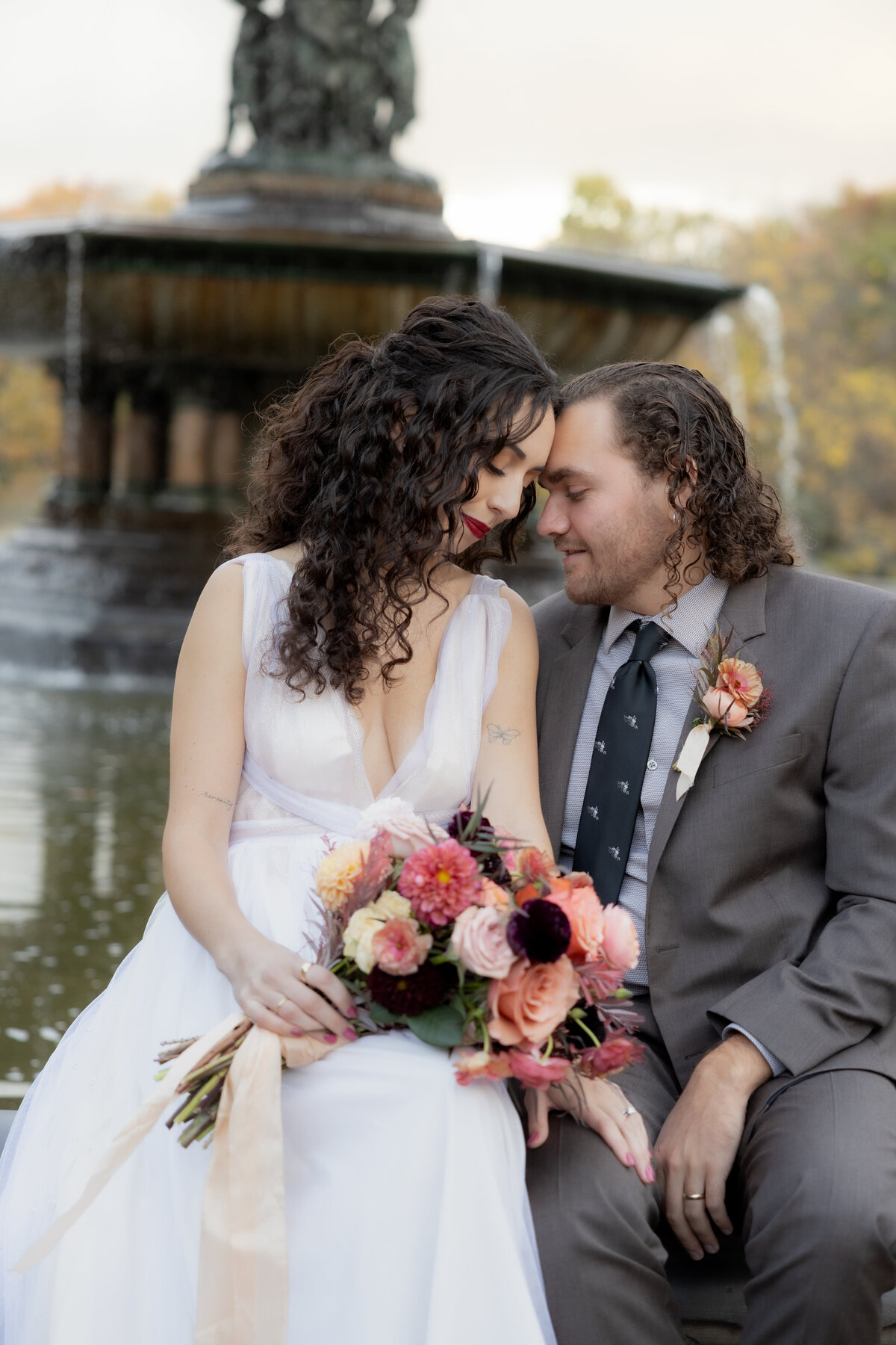 The couple standing close together surrounded by Central Park’s glowing fall foliage.