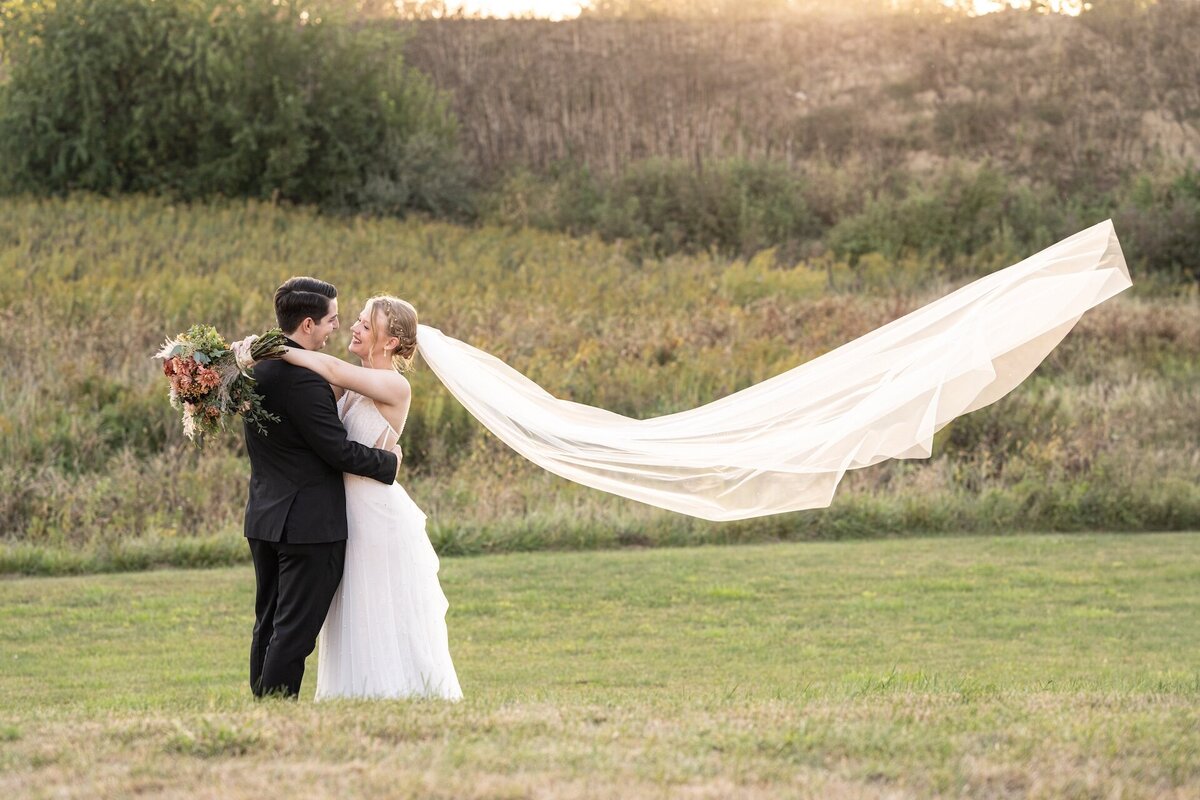newlyweds kissing in wedding attire with a sunset and trees in the background