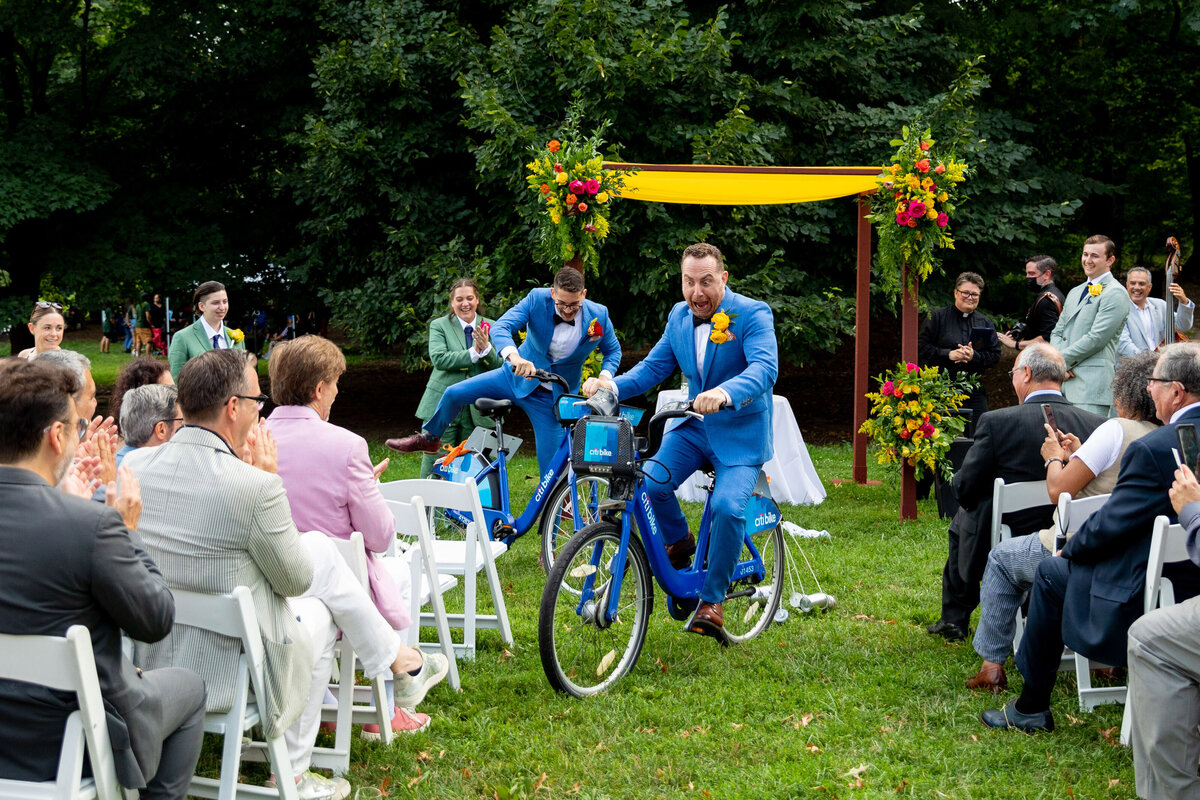 Two grooms riding bikes up the aisle.