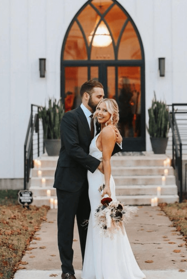 Bride with soft updo, natural makeup, and french manicure stands with groom after men's haircut and beard trim in Austin wedding setting