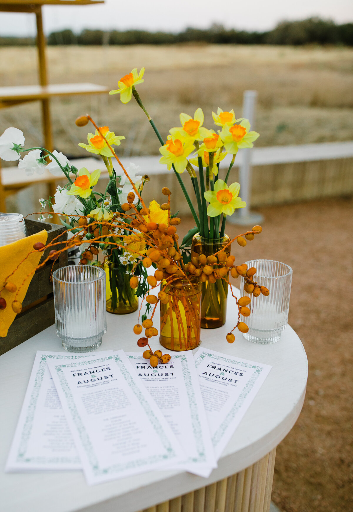 Table with wedding programs and bright yellow and orange florals