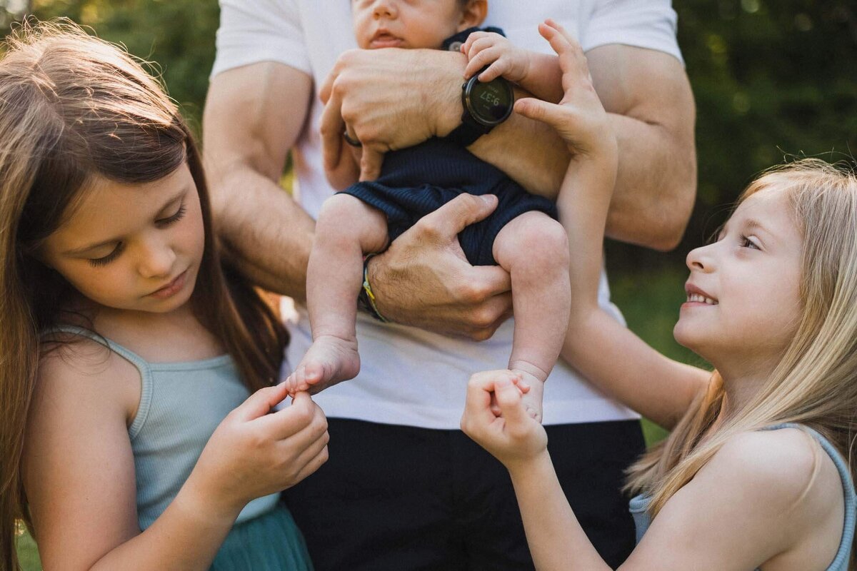 Sisters hold baby brother's toes during newborn photography session at Huntington Reservation in Cleveland.