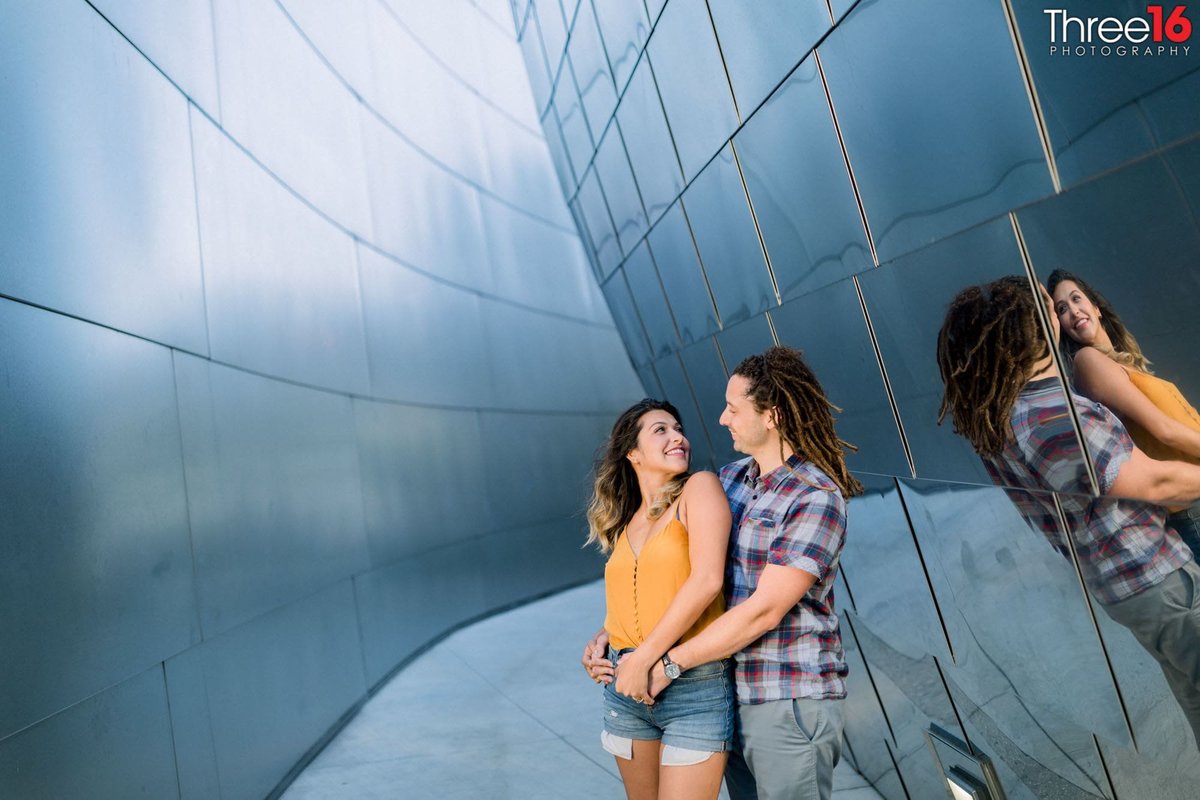 Groom to be holds his Bride from behind as she looks back at him during engagement session at the Walt Disney Concert Hall