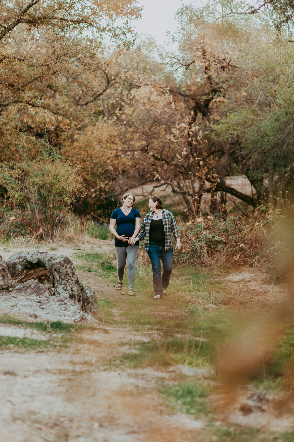 Same sex couple holds hands as they walk, one of the people is pregnant.