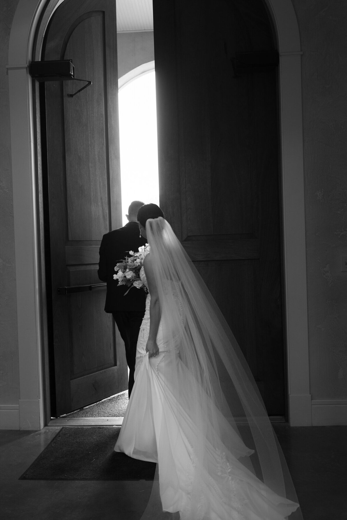 Bride walking with her groom through chapel doors in black and white