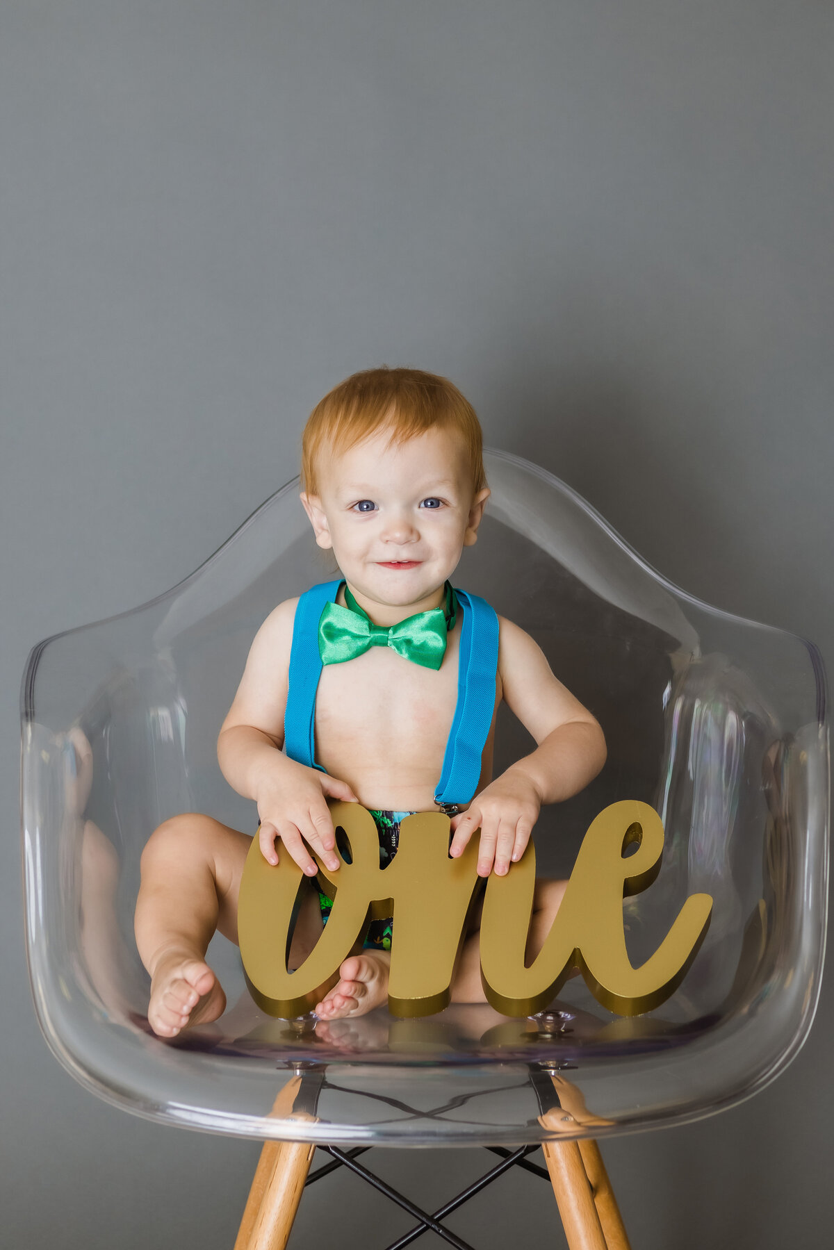 Cake Smash Photographer, a baby boy sits on a chair with carved word number one