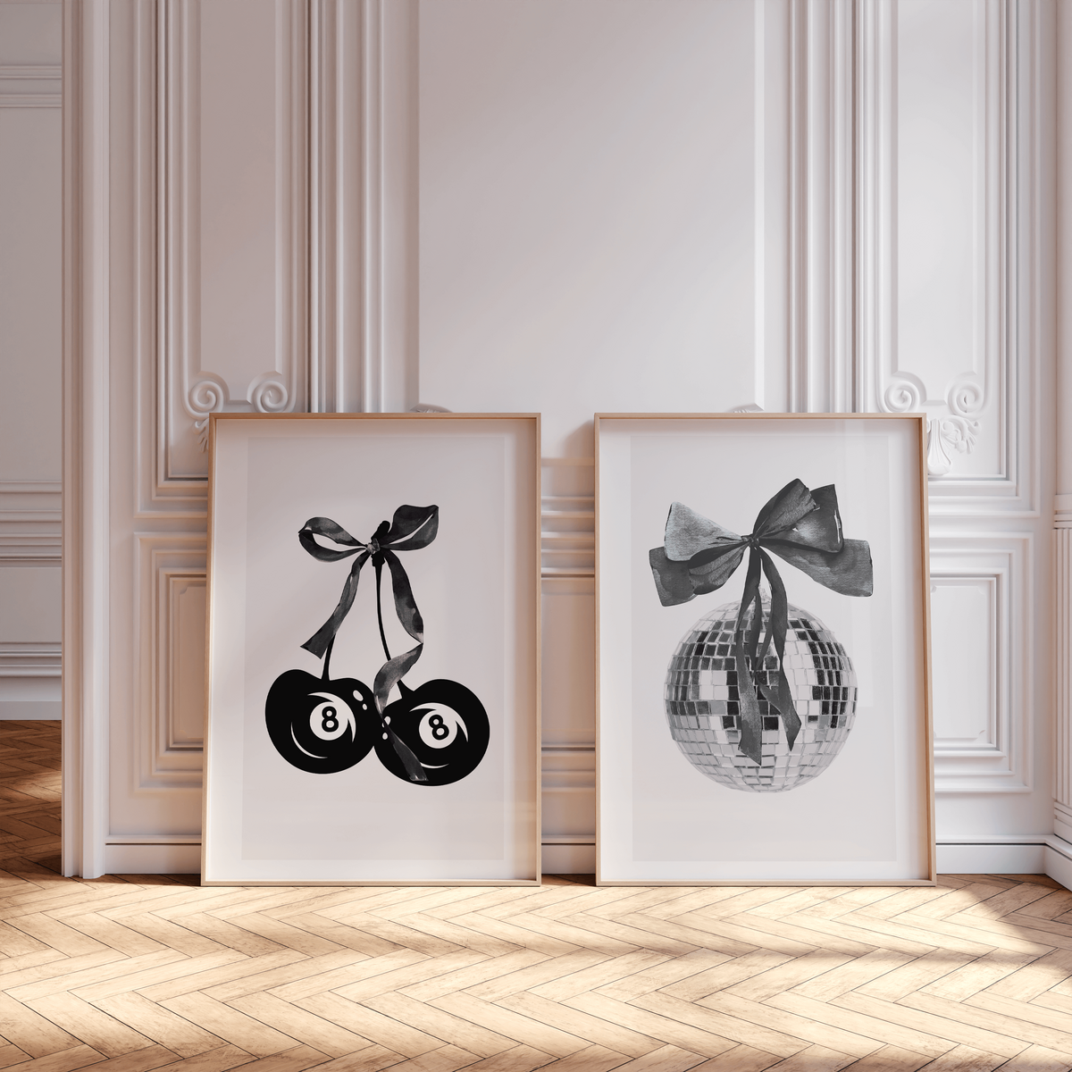 Two framed art prints by Sweet Pea Ink Design lean against a white ornate wall; one features billiard balls with a ribbon, the other shows a disco ball with a ribbon, reflecting modern brand design flair.