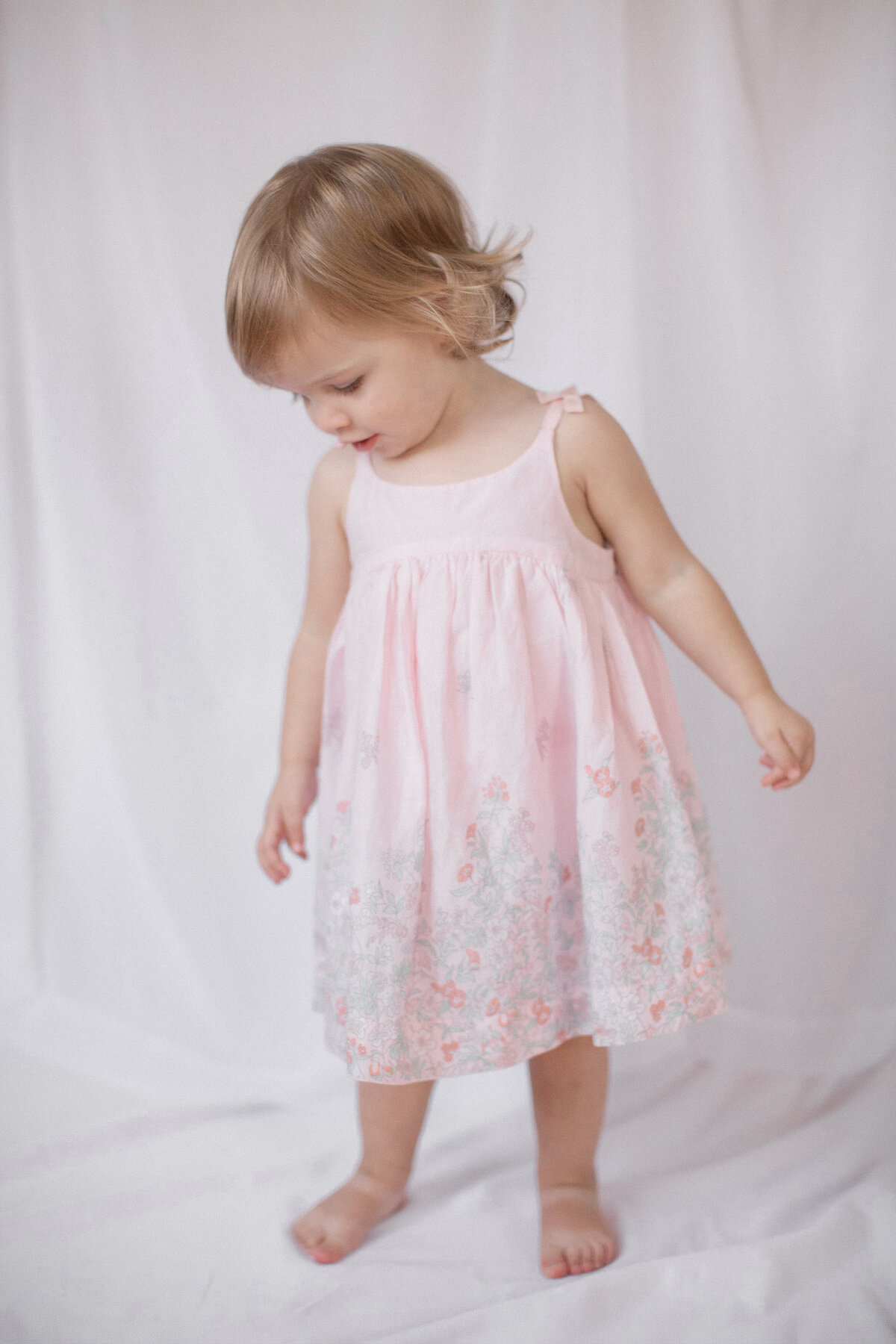 Toddler dances in pink dress in studio portrait.