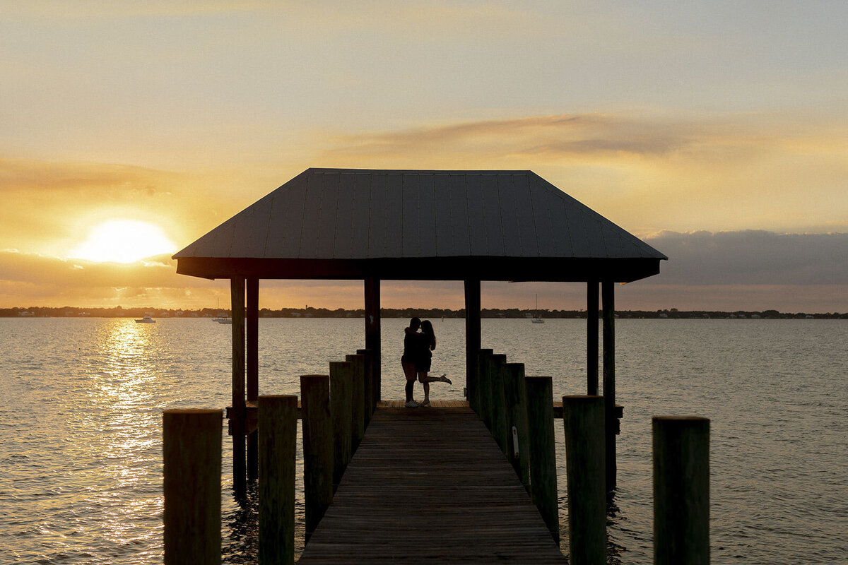 Couple kissing on a pier with sunset in the background