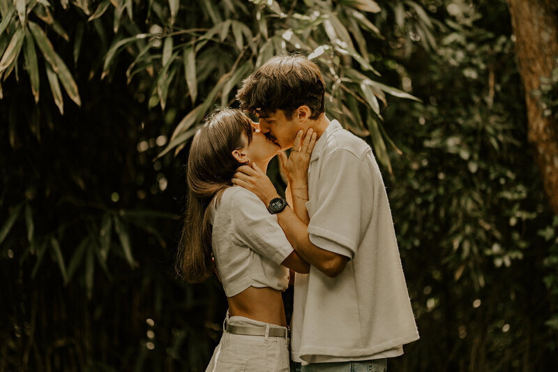 Couple se faisant un bisou devant un décor de feuilles exotiques lors d'un shooting photo couple.