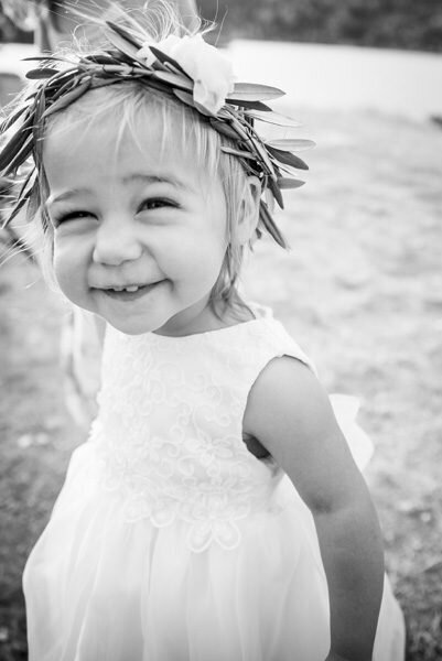 A small flower girl cheeses for the camera wearing a crown made of greenery.