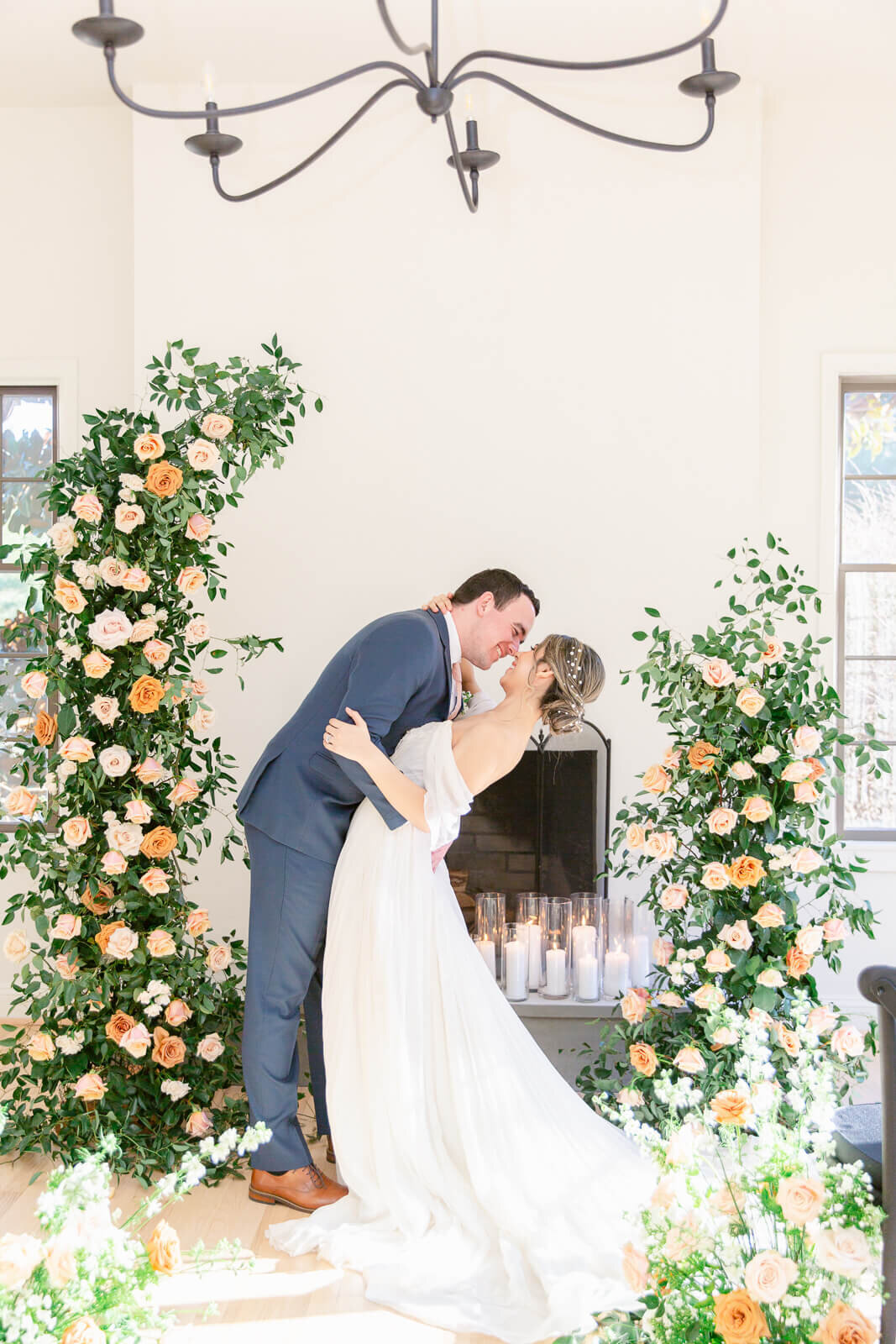 Handsome groom dips bride surrounded by gorgeous florals in front of a fireplace at Hemlock Hospitality, a beautiful Virginia wedding venue. Captured by Bethany Aubre Photography.