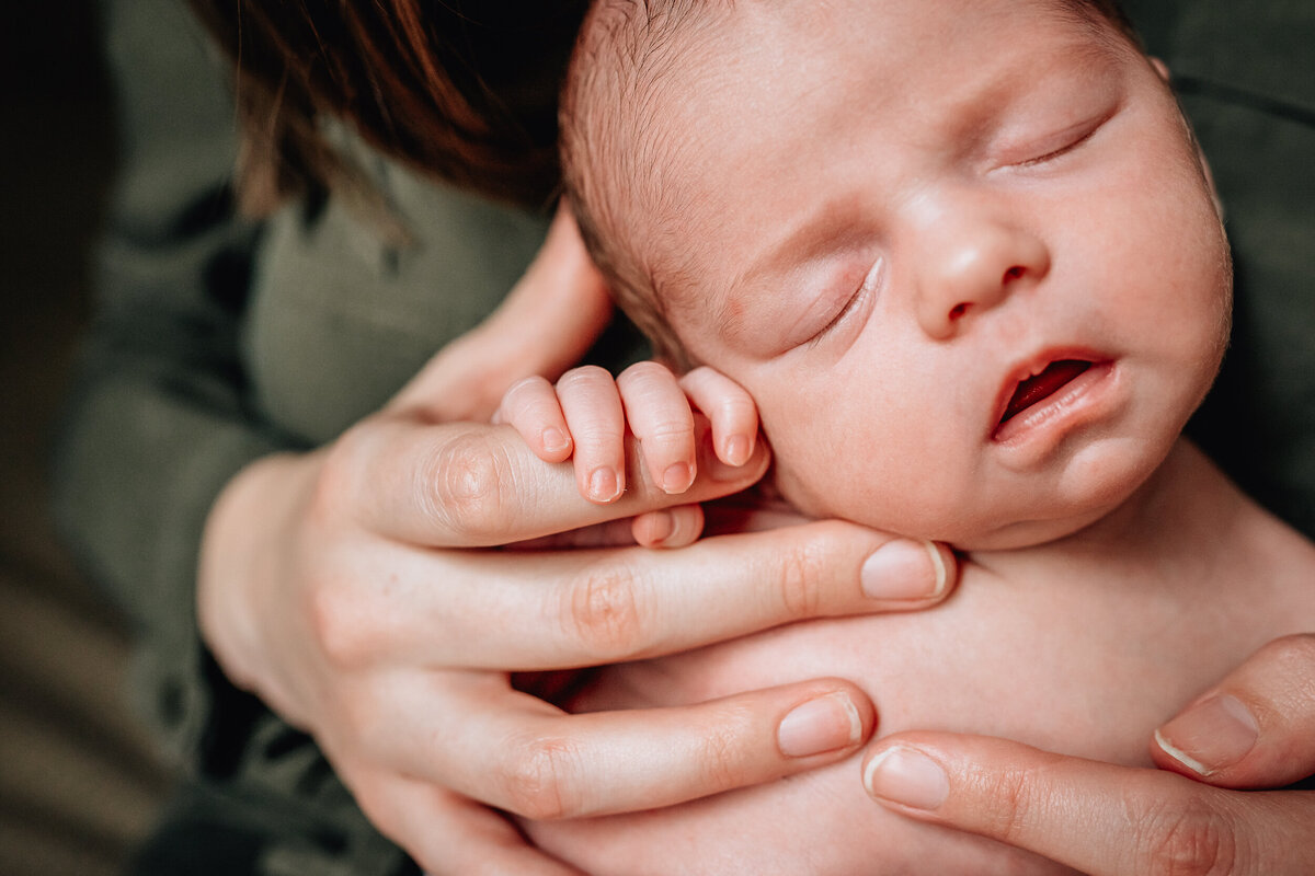 Close up of a newborn with their eyes closed being held by their mother.