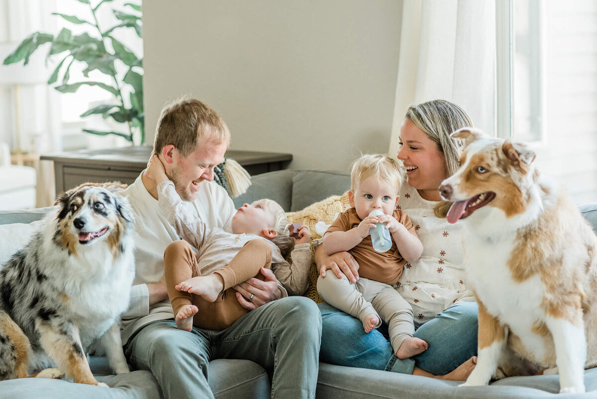 husband and wife on their couch with their two sons and two dogs while getting photographed for their WI wedding website in Oconomowoc Wisconsin