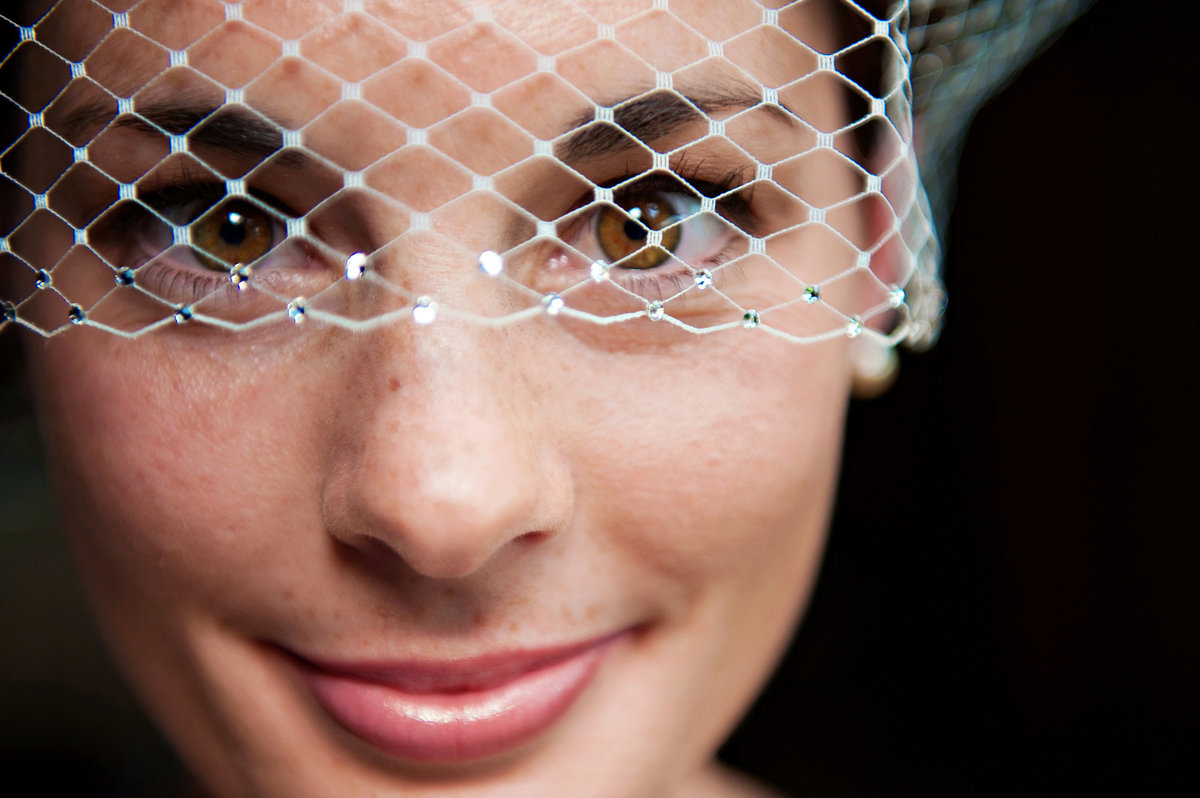 A beautiful bride in her birdcage veil before her rustic barn  wedding