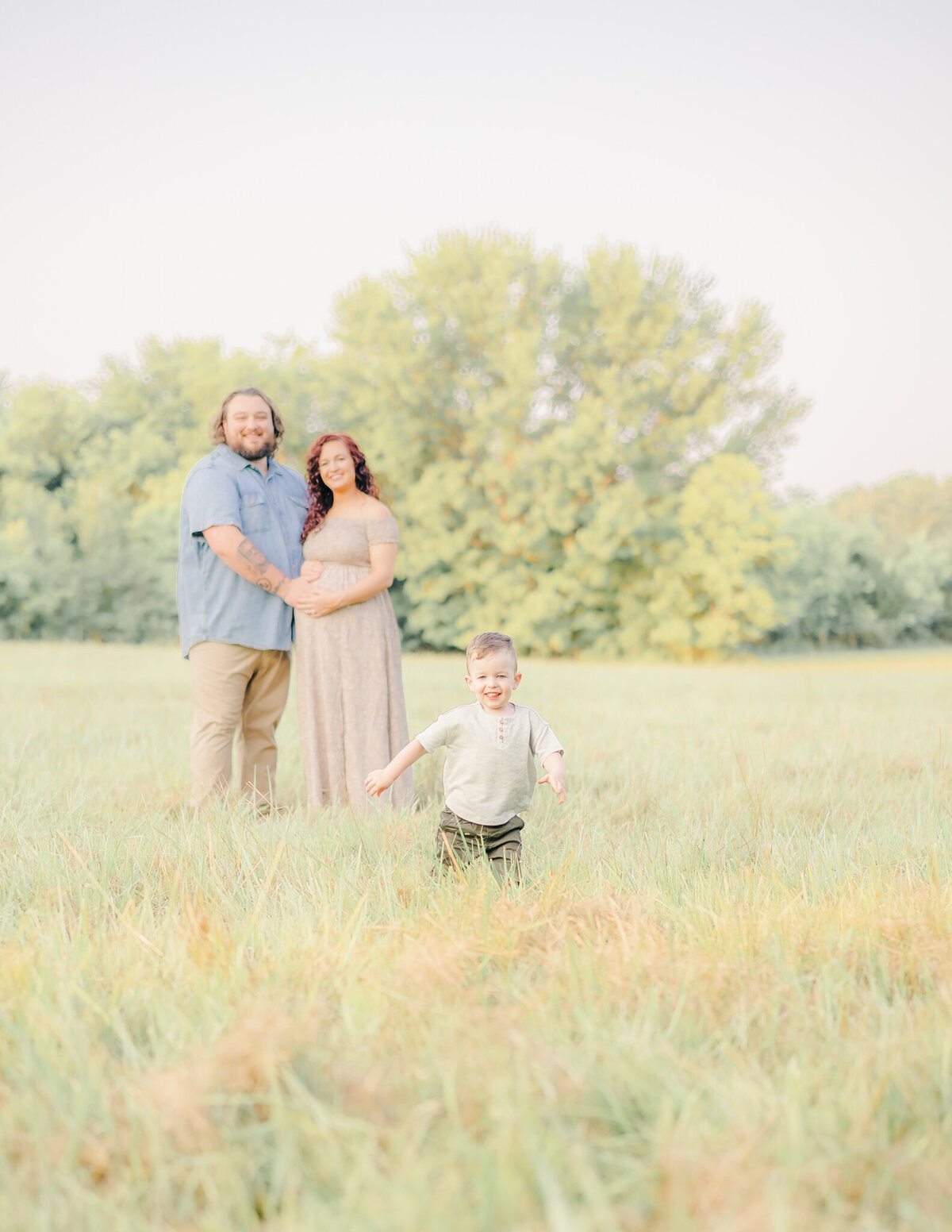 small toddler running from parents while they are posing in background in a field of tall grass