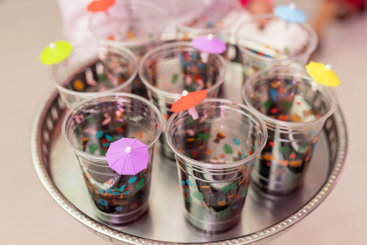 Clear plastic party cups filled with confetti and mini umbrellas on a silver tray