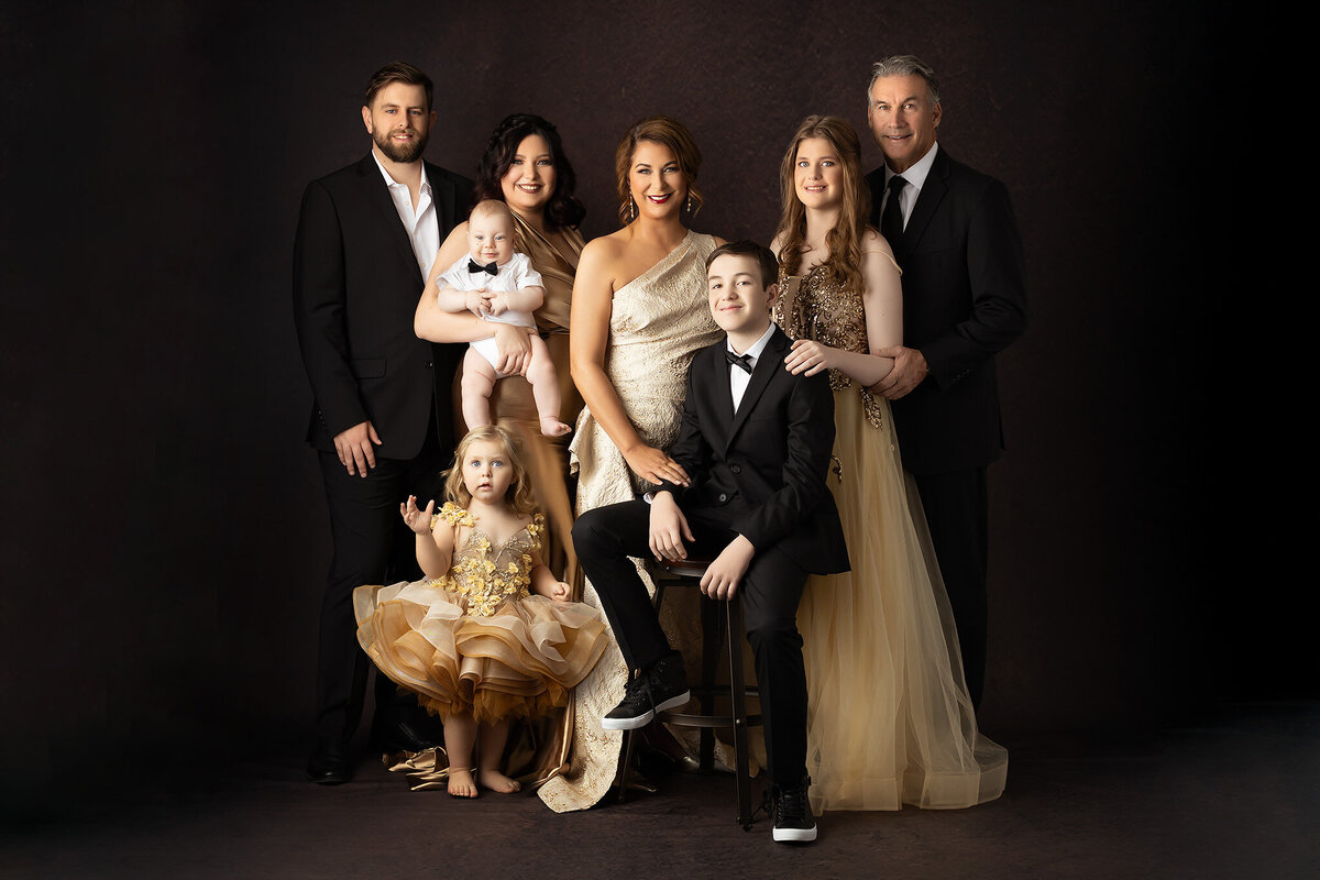 A beautiful family portrait featuring a couple in black tuxedos, a golden gown, and their children in matching outfits, taken by a Dallas family photographer.