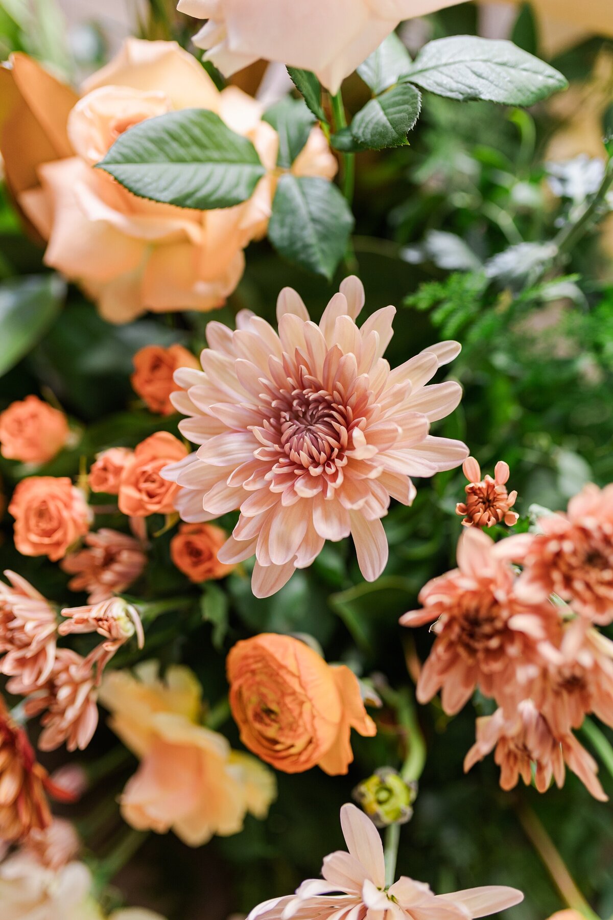 A detail shot of a wedding bouquet at a wedding in DFW, Texas. The flowers are all different shades of pink and orange and are surrounded by lots of greenery.