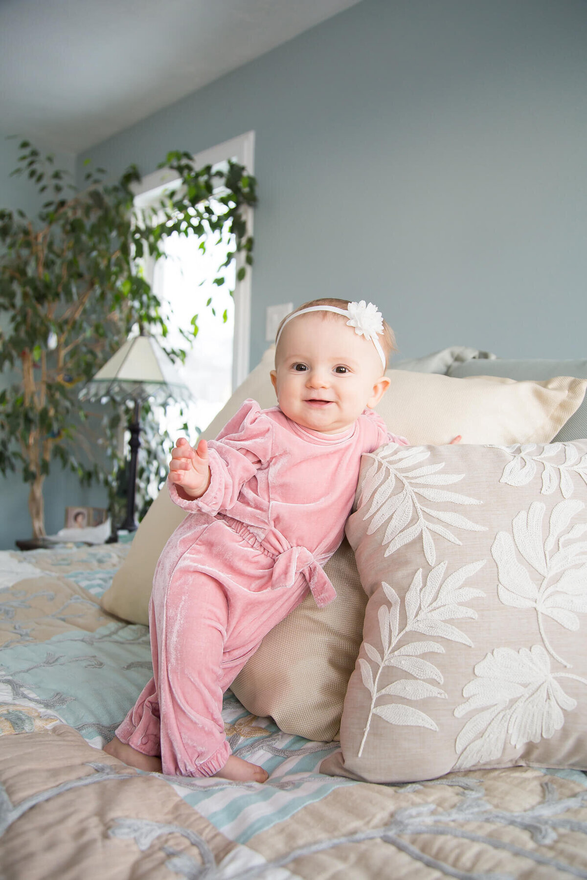 Happy one year old girl in pink velvet romper standingn on a bed