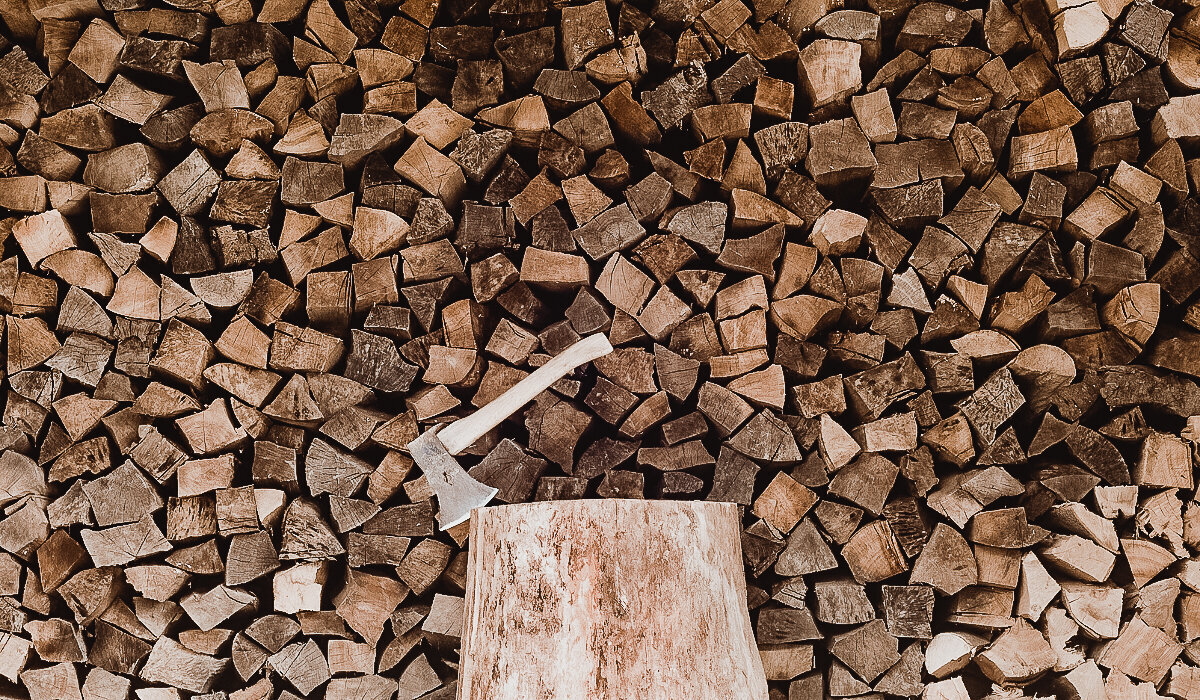Axe stuck in wood chopping block in front of stack of split firewood