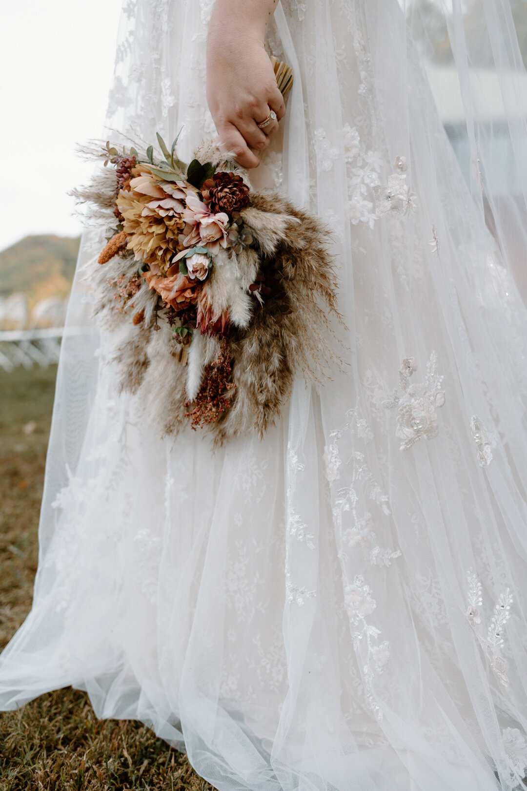 Boho bride carrying a fall bouquet with fall colors and feathers.