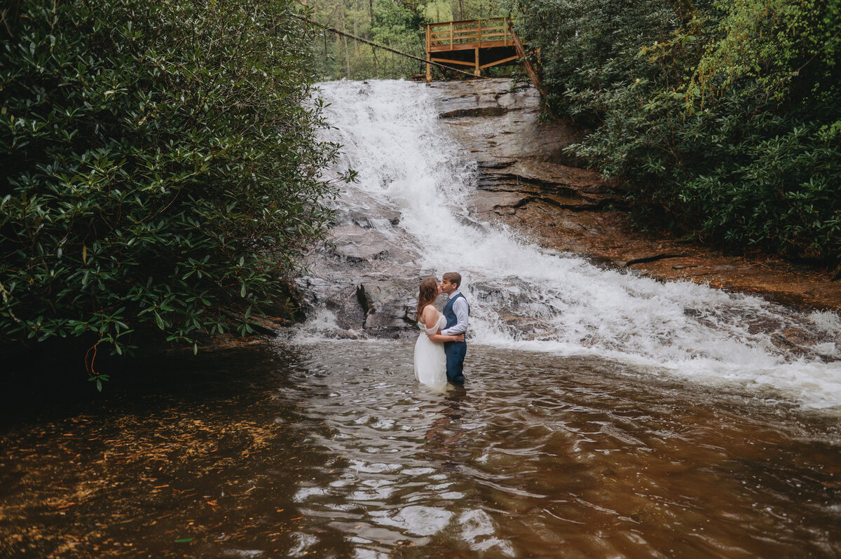 A couple leans in for a kiss while standing in the water