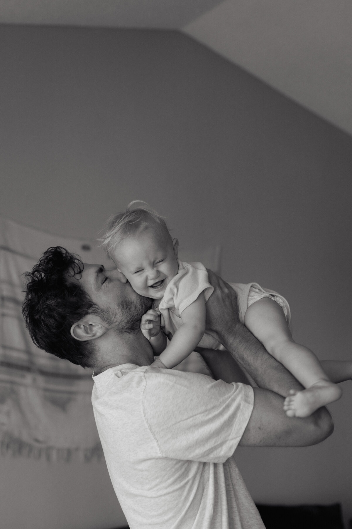 A father kissing his smiling baby, showcasing a heartwarming moment with a high-end documentary wedding photography approach.