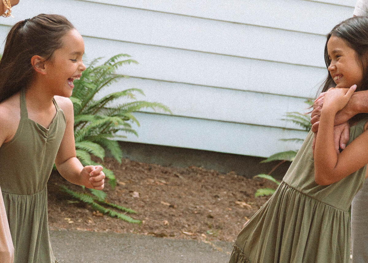 Two young sisters laughing together outside a white building during family photos in Irvine.