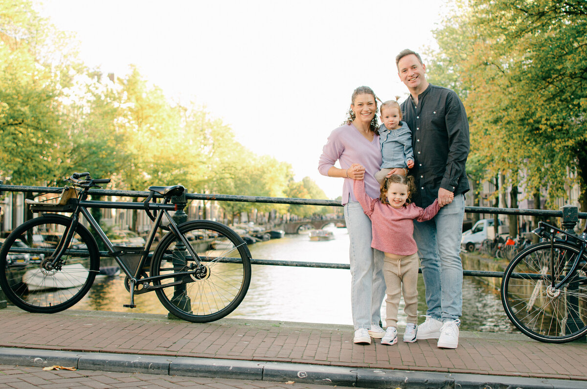 Family with young children standing on canal bridge in Amsterdam at sunset
