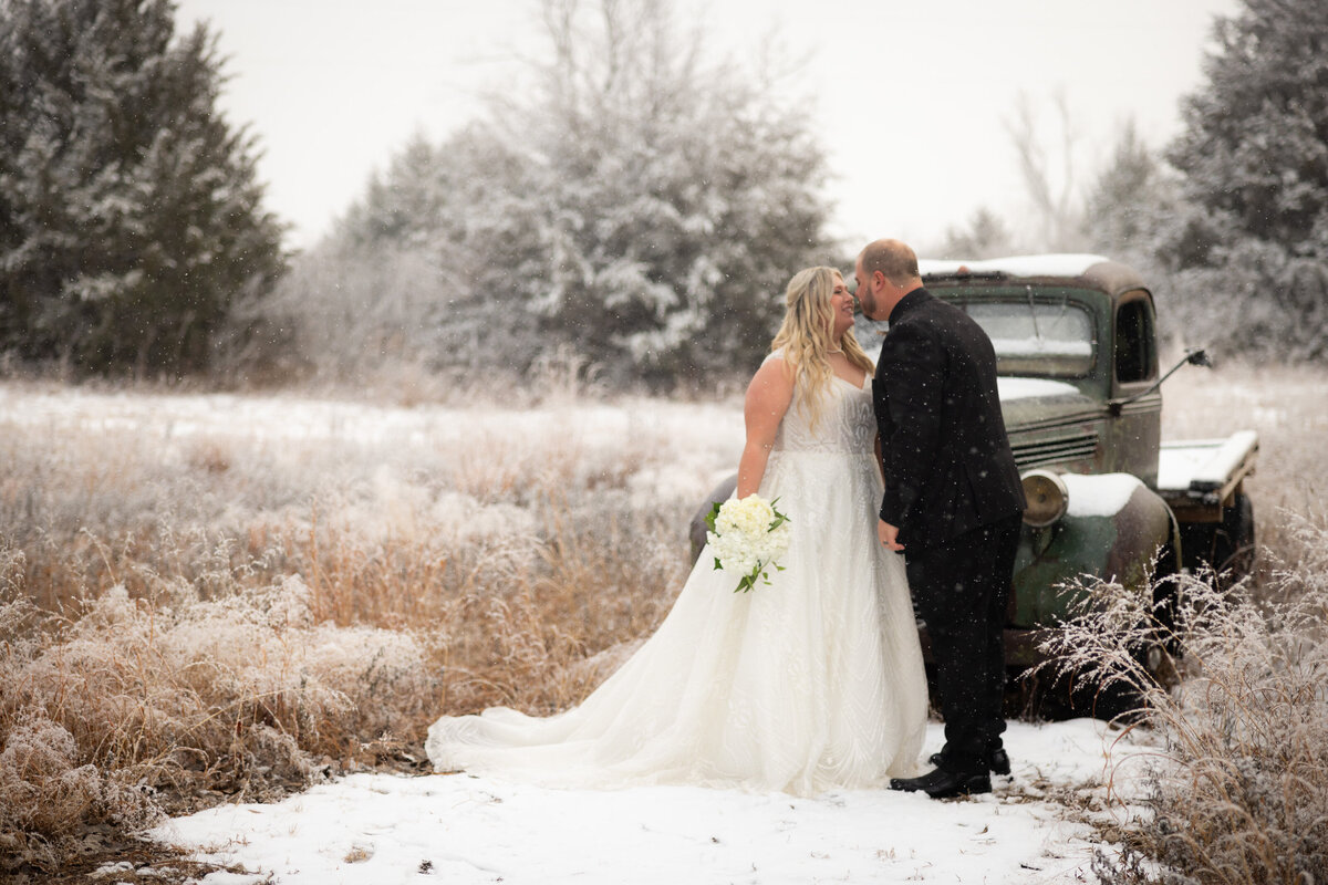 bride and groom kissing in front of snow covered old truck