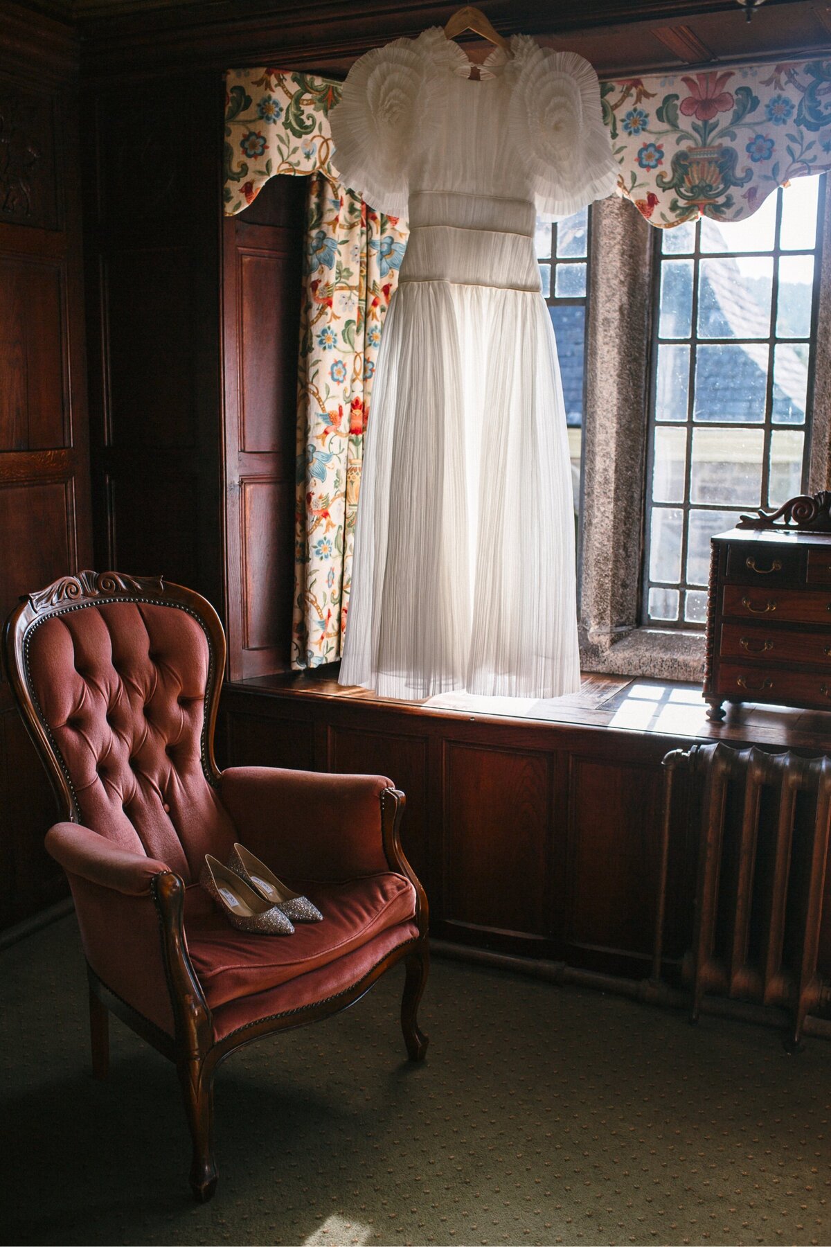 Wedding dress hangs in sunlight in regal style hotel room 