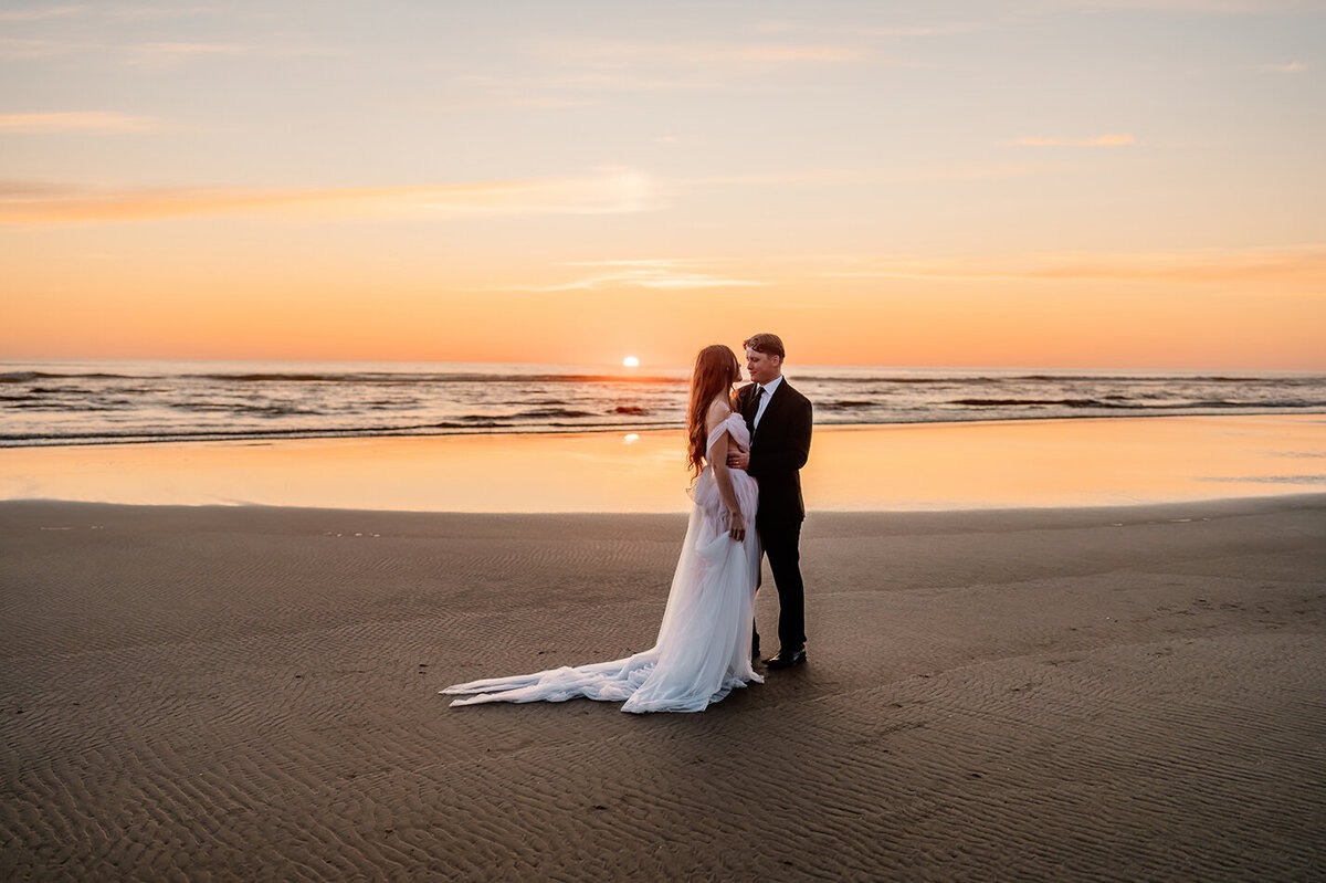 a couple on the beach in oregon, looking at each other during sunset