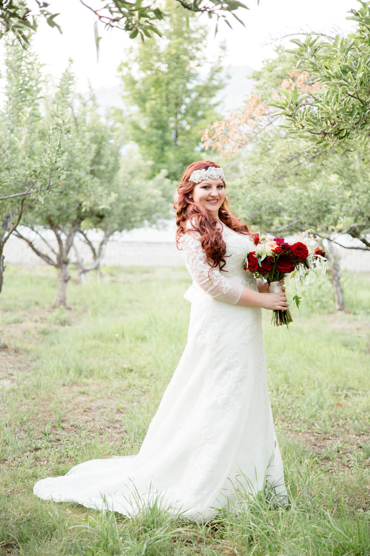 Beautiful Red headed bride standing with a bouquet in an apple orchard