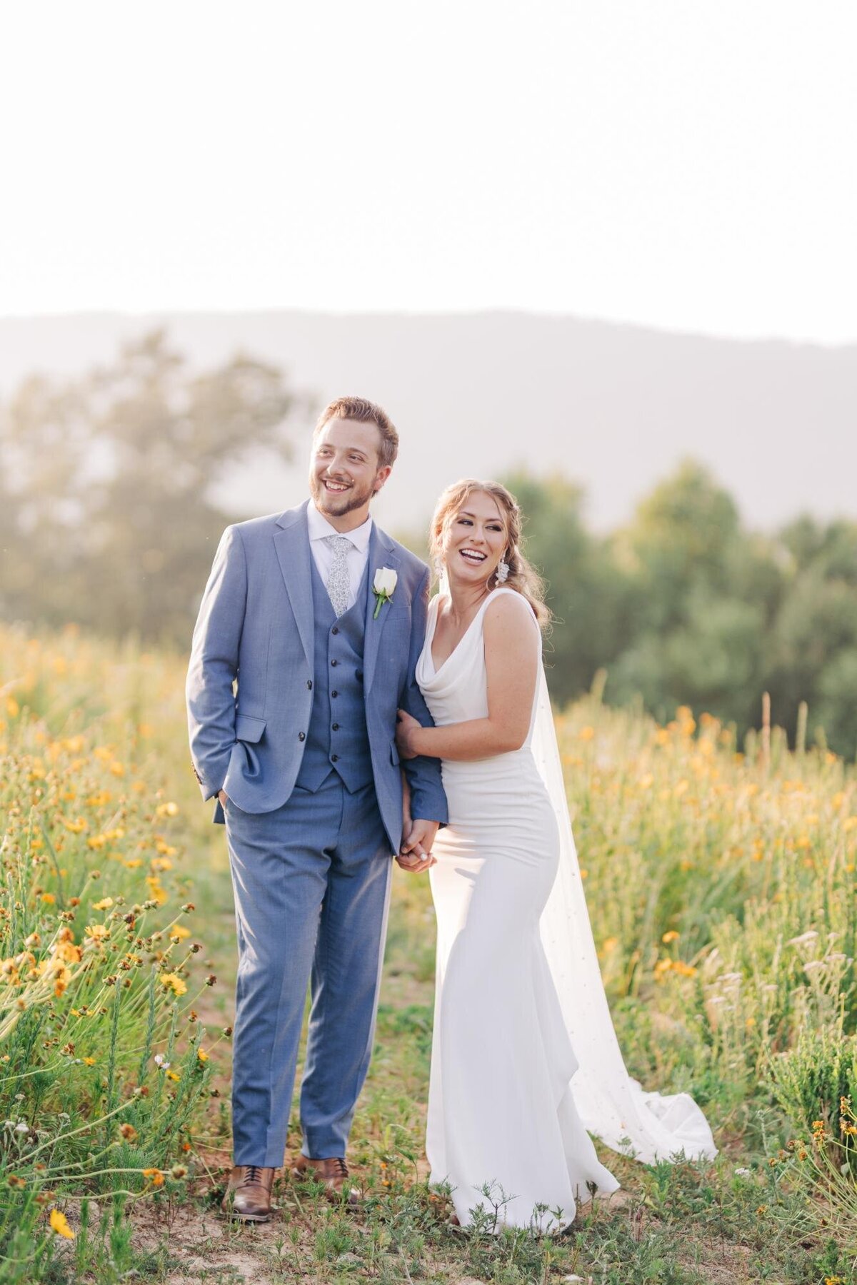 Bride and groom smiling in a field with wildflowers.