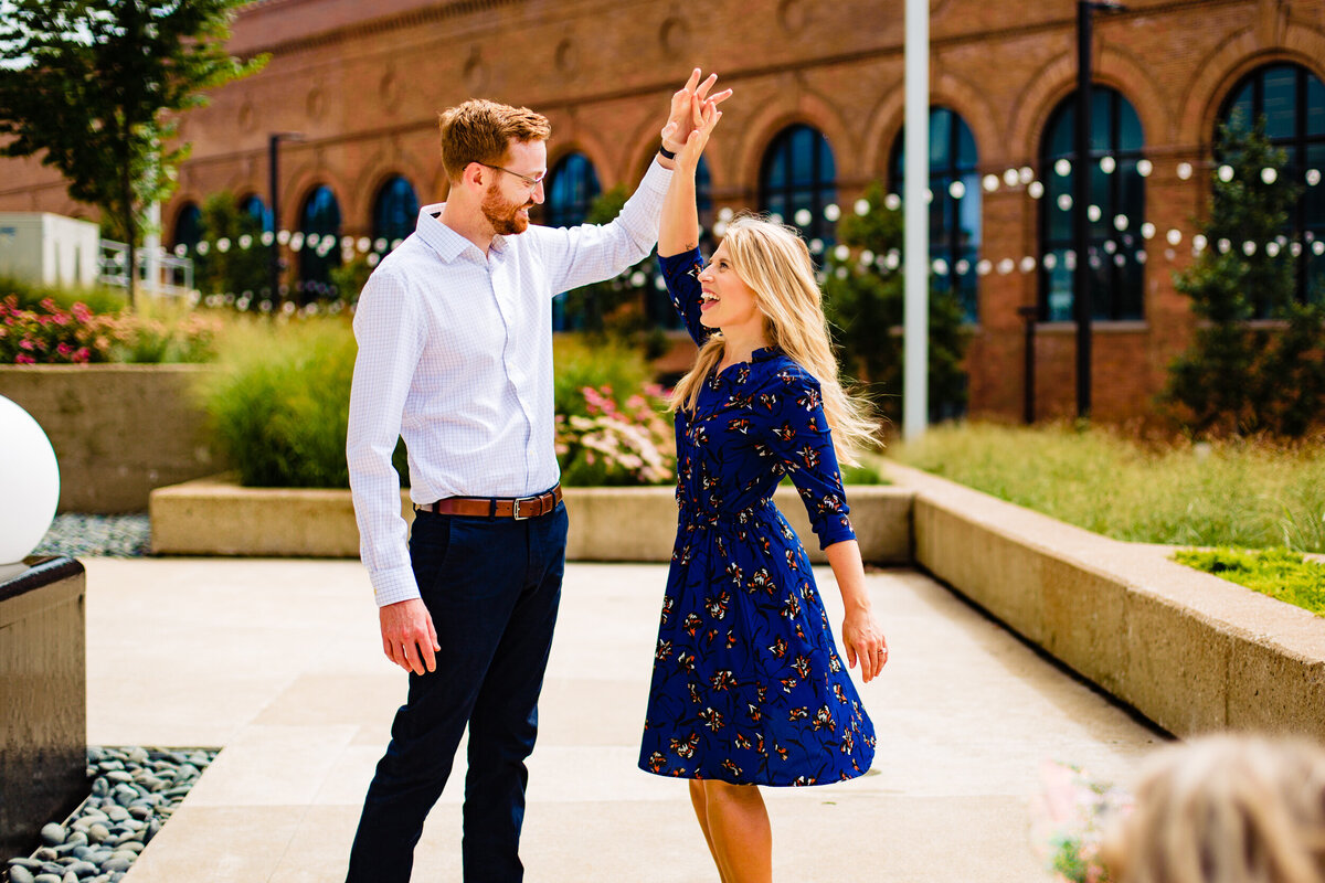 An engagement photo of a couple dancing in downtown Toledo Ohio. The bride spins in her blue dress while laughing.  Photo By Adore Wedding Photography. Toledo Wedding Photographers