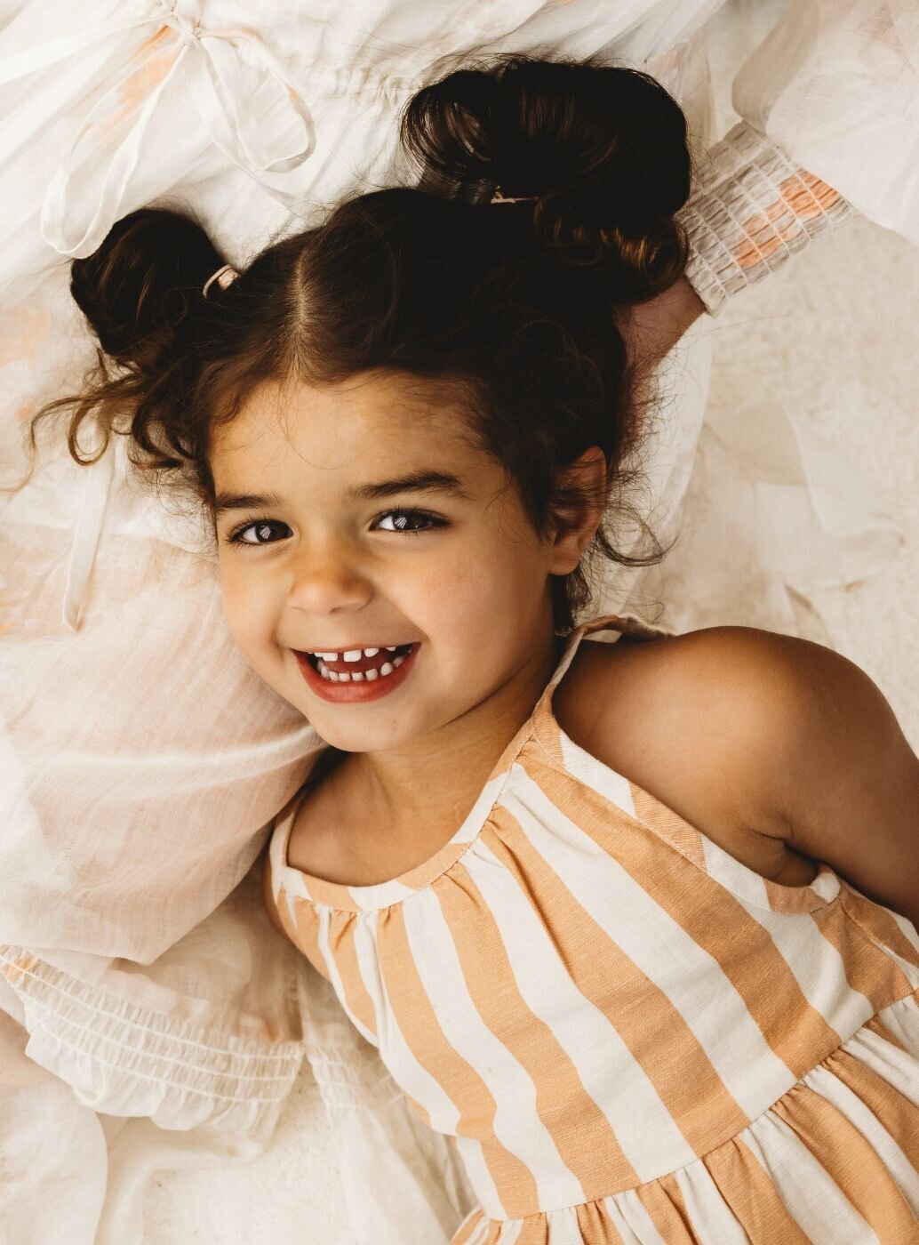 A girl wearing a stripe white and yellow dress laying down and smiling on a camera and she is so happy