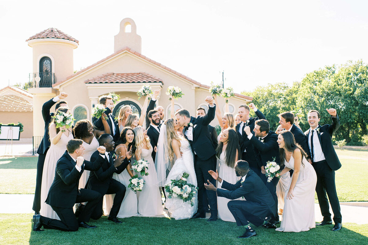 Wedding party celebrates while bride and groom kiss outside of D'Vine Grace Vineyard