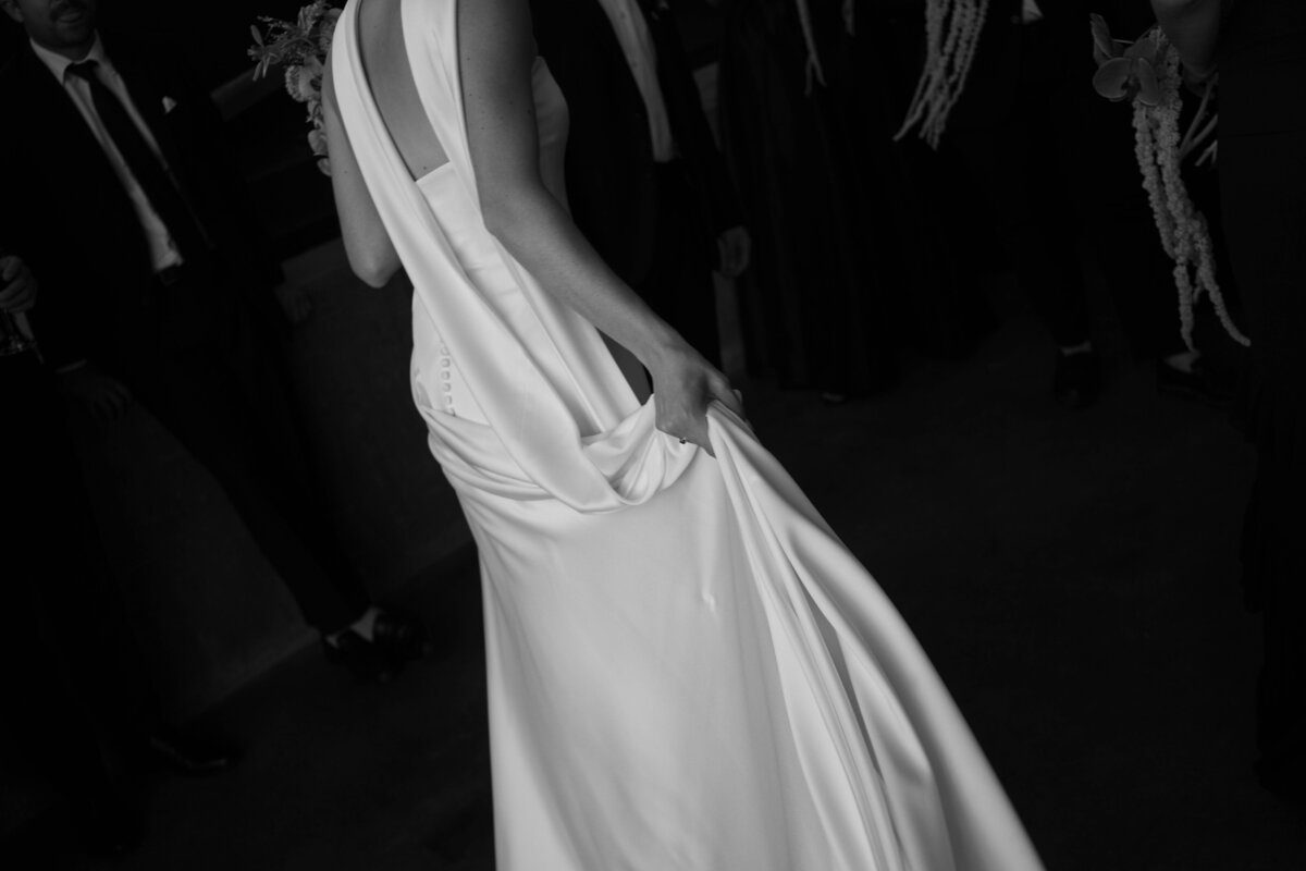 Bride holding satin gown while walking across dance floor in black and white photo