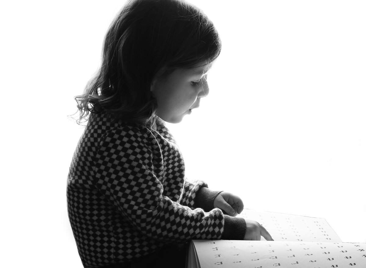 Black and white portrait. Little boy is seen reading a book in Hebrew. Captured by brooklyn family photographer Chaya Bornstein.