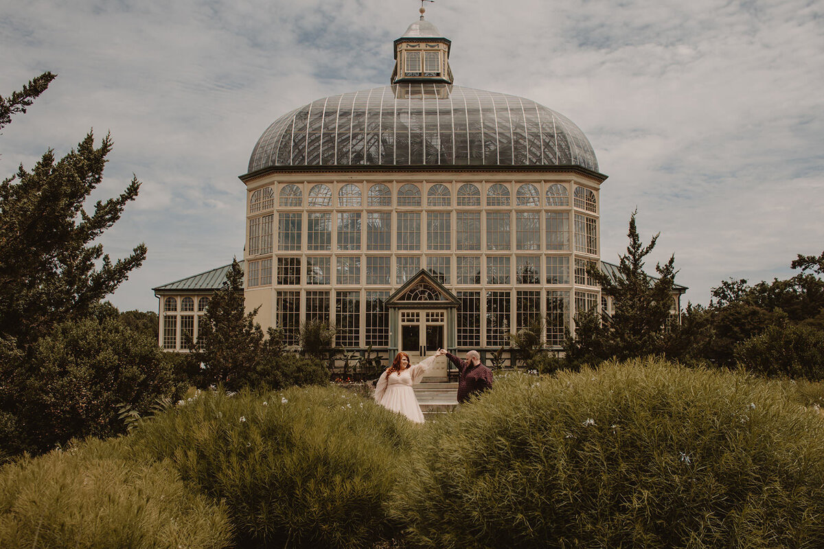 A couple dancing together in front of a large greenhouse