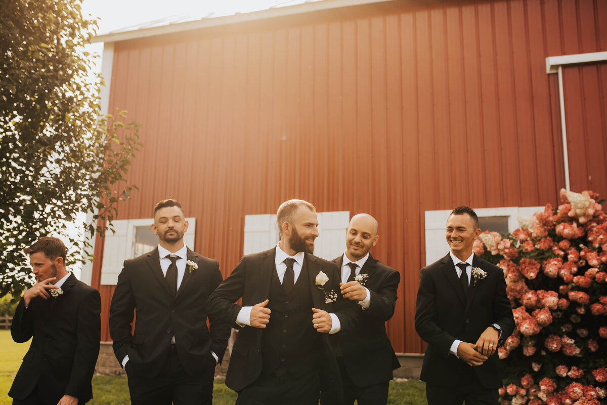 groom walking with his groomsmen in front of a red barn