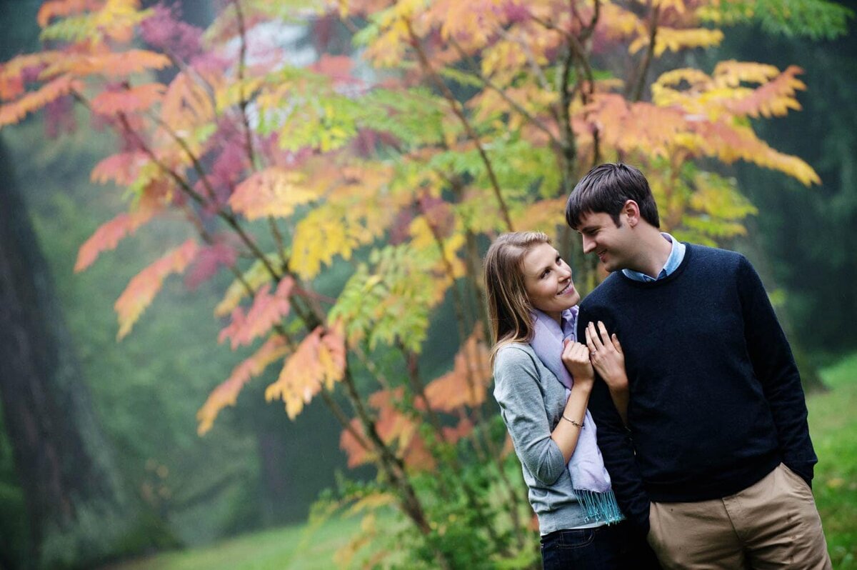a man and woman look at each other standing in front of a multicolored tree