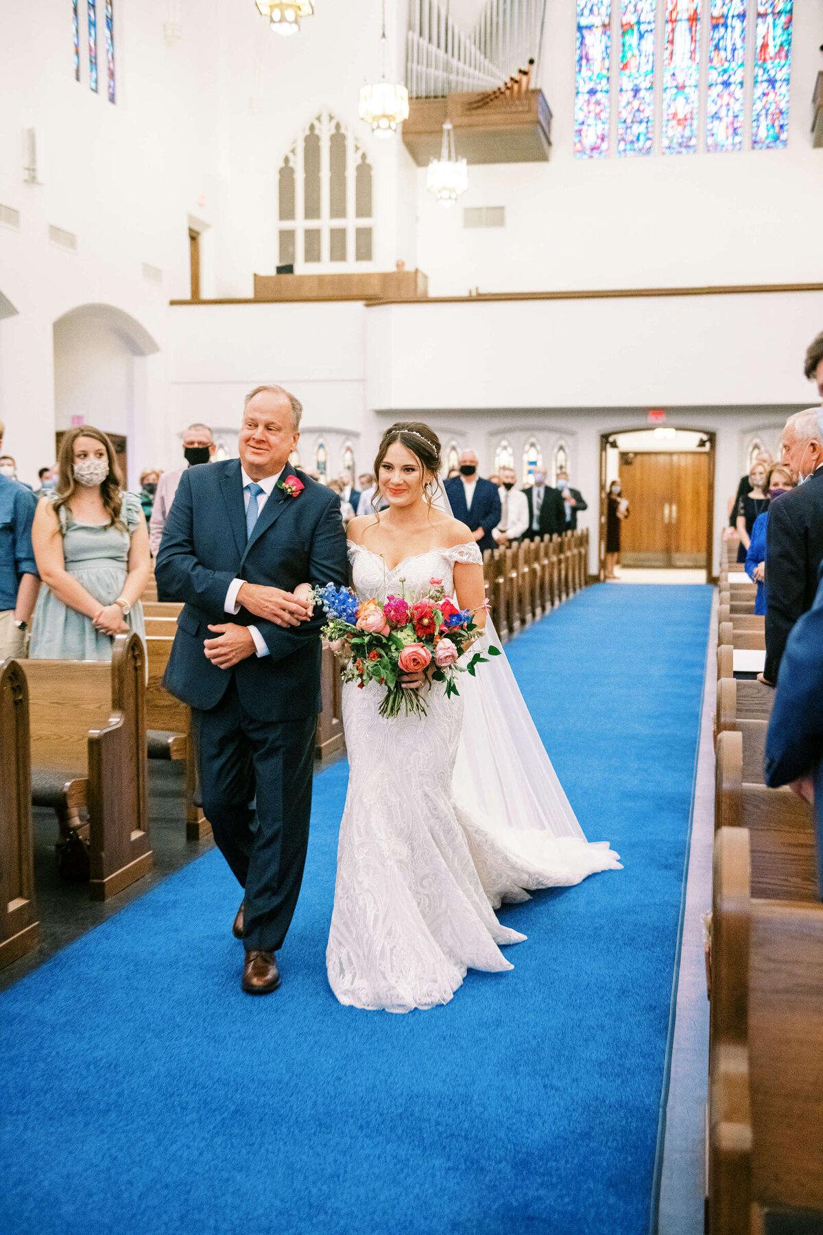 Father of the bride and bride walk down aisle at The 4Eleven venue with colorful bouquet