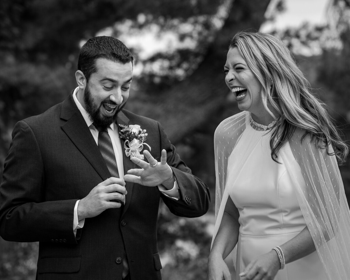 Black and white photo of bride and groom looking at his ring during a candid ceremony moment, an award-winning image by Fox & Brazen.