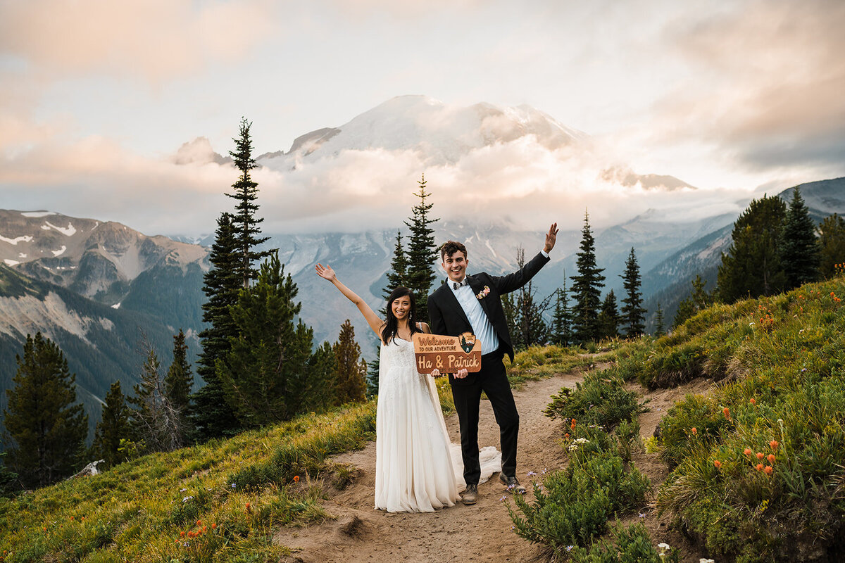 Bride & groom posing in front of Mount Rainier with a National Park sign custom made for their elopement day!