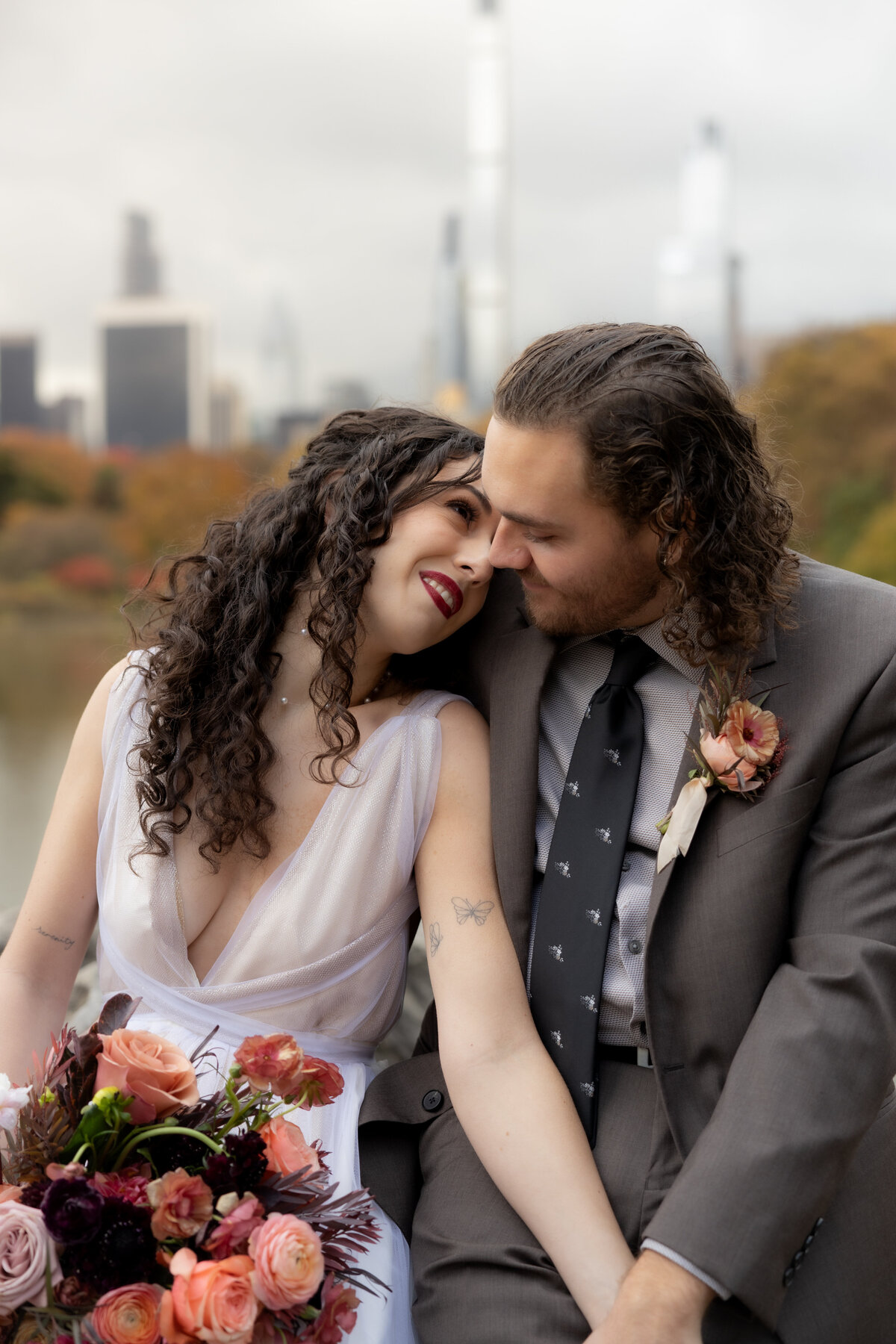 The couple standing close together surrounded by Central Park’s glowing fall foliage.