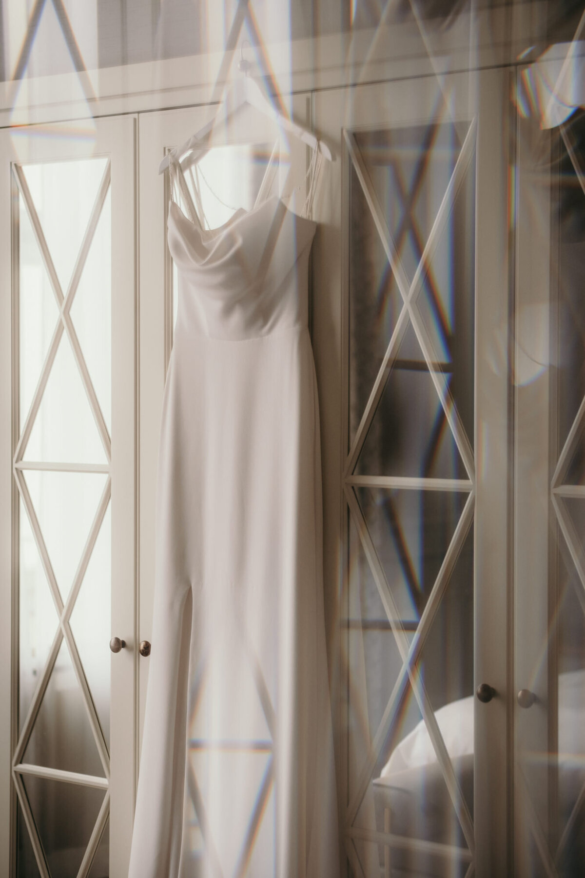 Das Brautkleid hängt an einem verspiegelten Kleiderschrank auf einem Kleiderbügel.