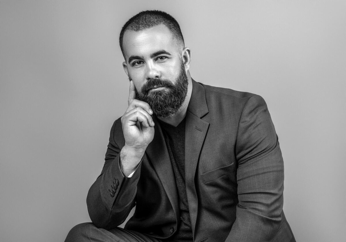 Black and white portrait of a bearded man in a suit, resting his chin on his hand.